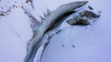 Dağlardaki bir buzuldan dev bir buz duvarı. Her yer kar ve büyük taşlarla kaplı. Buzdaki çatlaklardaki dronun üst görüntüsü. Buzul kırılır, buz kırılır. Almaty