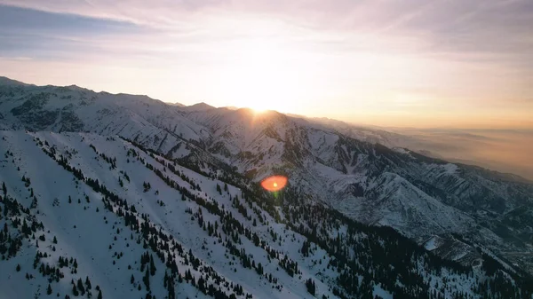 stock image Epic red-orange sunset in high snowy mountains. There are tall coniferous trees, there is snow on the hills. High peaks. The suns rays fall on the clouds and fog that is lower down the gorge. Almaty