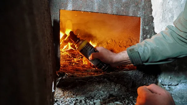 The guy lights a fire in the oven. To lay firewood. An old stove in an abandoned hut. Rusty metal doors. Dirty dusty walls. Firewood and fuel briquettes are burning. Heat from the oven.