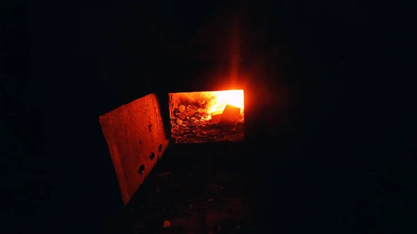 火が壁の古いストーブの中で燃えている ドアに錆びた金属 湿った凍結灰色の壁 床の上のゴミ 放棄された小屋と元刑務所 — ストック写真
