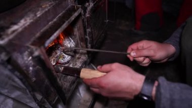 Kamp fırınından fırında pişmiş patatesleri folyoyla çıkarıyorum. Patatesler kömür ve ateşte pişirildi. Bıçak ve çadır kazığı kullanıyorum. Soba çadırın içinde. Patatesler hazır. Duman var.