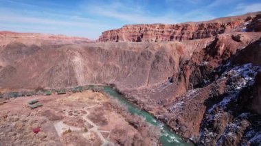 Charyn Kanyonu 'nda yeşil suyu olan uzun bir nehir. Bazı yerlerde beyaz kar var. Çalılar ve ağaçlar büyür. Nehir kayaların ve kayalıkların arasındaki bir kanyondan geçiyor. Dağlar görünür. Drone görünümü