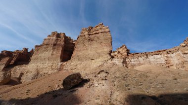 Büyük Kanyon Charyn. Turuncu uçurumlar ve kayalar. Bazı yerlerde kuru çalılar ve kar vardır. Güneş ışıl ışıl parlıyor. Beyaz bulutlar. Kanyondaki hatalar ve çatlaklar. Burası Mars 'a benziyor.