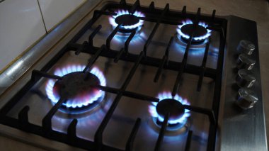 Gaz sobasında mavi bir ateş yanıyor. Benzin evde. Metal gaz sobası. Siyah çubuklar. Kullan-at telefonları aç. Gaz işe yarıyor. Duvarlarda bej fayanslar var. Ekonomik krizi durdurun. Evdeki sıcaklık.