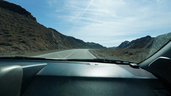 stock image View of the road through the windshield. Cars are passing by. There are high rocky hills around the edges. Everything is covered with small dry bushes. There are dry trees and poles. White clouds