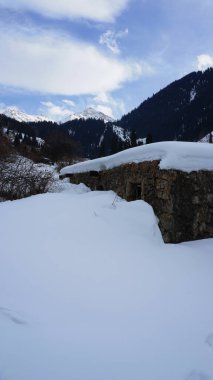 Dağlarda eski bir taş hapishane ya da kulübe. Karlı dağlar, orman ve bulutlar mavi gökyüzüne karşı. Uzun kuru çalılar karların altından dışarı bakıyor. Huş ağacı ve çam ağaçları uzaktan görülebilir..