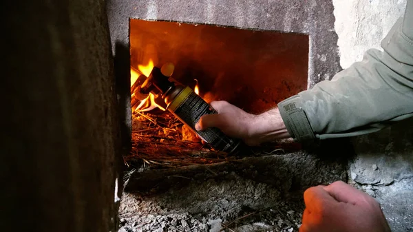 The guy lights a fire in the oven. To lay firewood. An old stove in an abandoned hut. Rusty metal doors. Dirty dusty walls. Firewood and fuel briquettes are burning. Heat from the oven.