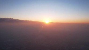 Efsanevi gri sis, gün batımında şehrin üzerinde görülebilir. Evlerin, yolların, arabaların ve parkların insansız hava aracından kuşbakışı görüntüsü. Beyaz bulutlar ve karlı dağlar güneşin turuncu ışınlarıyla aydınlatılır. Almaty