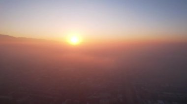 Efsanevi gri sis, gün batımında şehrin üzerinde görülebilir. Evlerin, yolların, arabaların ve parkların insansız hava aracından kuşbakışı görüntüsü. Beyaz bulutlar ve karlı dağlar güneşin turuncu ışınlarıyla aydınlatılır. Almaty