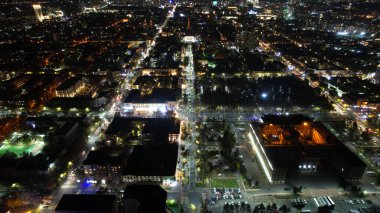 Gece şehrinde büyük bir konser. Kalabalığın insansız görüntüsü, ışınları ve ışık huzmeleri. Işıklı büyük bir bina. Arabalı yollar, yayalı sokaklar ve etrafta bir park var.