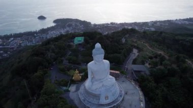 Büyük Buda, gün batımını seyrediyor. Phuket. İnsanlar heykele çıkan basamakları tırmanıyor. Adanın yeşil tepeleri her yerde. Uzakta, parlak güneş denizin üzerinde gider. Yukarıdan görüntüle