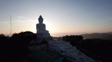 Büyük Buda, gün batımını seyrediyor. Phuket. İnsanlar heykele çıkan basamakları tırmanıyor. Adanın yeşil tepeleri her yerde. Uzakta, parlak güneş denizin üzerinde gider. Yukarıdan görüntüle