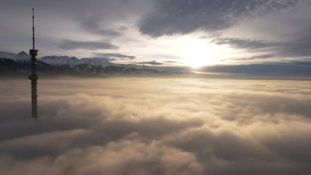 テレビ塔は日没時に雲の外を見る 雲の二重の層のドローンからの上の眺め 太陽の光による黄橙色 雲の上の影 遠くの高い山 — ストック動画