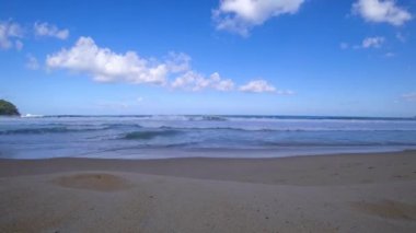 Okyanus manzaralı gün doğumu zamanı, mavi gökyüzü ve beyaz bulutlar. İnsanlar rahatlıyor, sahilde yürüyorlar. Bulutlar uçuyor. Mavi denizde büyük dalgalar. Bulutların gölgesi. Karon Sahili