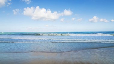 Beyaz bulutlu altın kum ve mavi okyanus suyu. Karon Sahili. Bazı yerlerde, yüksek dalgalar ve sıçramalar. Mavi gökyüzü. Güneş ışınları kuma yansıyor. Dalgalardan beyaz köpük. Tayland