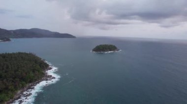 Okyanusun ortasındaki yeşil bir adanın en üst görüntüsü. Bulutlardan koyu yeşil su. Gün batımı. Dalgalar adanın kayalarına vuruyor. Dalgalı deniz. İnsansız hava aracının görüntüsü. Karon Sahili, Phuket