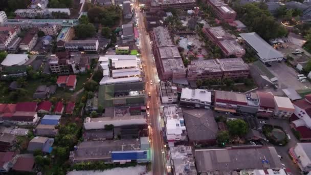 プーケット島 日没のカロン市のトップビュー プール付きの美しいホテルがあります 道路上の提灯やお店の窓が点灯します 車やオートバイのドライブ 緑の熱帯の丘 — ストック動画