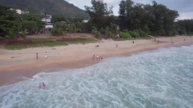 Deniz manzaralı ve bulutlu güzel bir gün batımı. Kumlu bir sahil ve su üzerindeki bir dronun üst görüntüsü. Turistler rahatlar ve yüzerler. Phuket Adası, Tayland 'ın yeşil tepeleri. Evler ve yüksek palmiye ağaçları