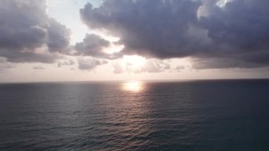 Deniz manzaralı ve bulutlu güzel bir gün batımı. Kumlu bir sahil ve su üzerindeki bir dronun üst görüntüsü. Turistler rahatlar ve yüzerler. Phuket Adası, Tayland 'ın yeşil tepeleri. Evler ve yüksek palmiye ağaçları