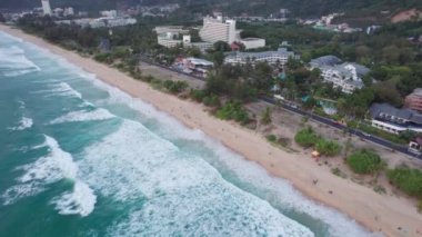 Deniz manzaralı ve bulutlu güzel bir gün batımı. Kumlu bir sahil ve su üzerindeki bir dronun üst görüntüsü. Turistler rahatlar ve yüzerler. Phuket Adası, Tayland 'ın yeşil tepeleri. Evler ve yüksek palmiye ağaçları