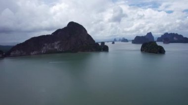 Uzun kuyruklu bir Tayland gemisi Phang Nga adaları arasında yelken açar. Yüksek kireçtaşı kayalıkları yeşil ağaçlarla kaplıdır. Mekanlar plajları ve mağaraları görebilir. Teknedeki turistler. Suda bir ayak izi.