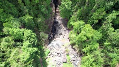 Kayaların ve yeşil ormanların arasında küçük bir şelale. Gökyüzünde bulutların yansıması olan küçük bir göl. Bir sürü ağaç. Yüksek uçurumlar ve büyük kayalar. Ağaçların gölgeleri. İHA 'nın üst görüntüsü. Tayland, Phuket