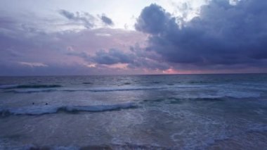 İnsansız hava aracından denizin üzerinde dramatik bir gün batımı. Karanlık su ve dalgaların en üst görüntüsü. Bulutların menekşe mavisi rengi. Uzakta ıssız bir ada. Kumsal. Güneş ışınlarının suya yansıması.