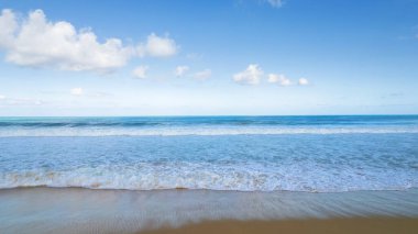 Beyaz bulutlu altın kum ve mavi okyanus suyu. Karon Sahili. Bazı yerlerde, yüksek dalgalar ve sıçramalar. Mavi gökyüzü. Güneş ışınları kuma yansıyor. Dalgalardan beyaz köpük. Tayland