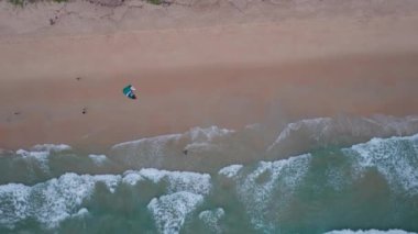 Okyanusun dalgalarında uçurtma sörfü yapan bir adam. Yeşil şeffaf su. Sarı kum. İHA 'dan paraglider' a üst görünüm. Tahta suda kayıyor. Büyük yeşil ada Phuket