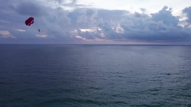 日没時にボートに縛られたパラシュートで飛ぶ 青いヴァイオレットの夕日 巨大な雲と暗い海の水 水の中の雲の反射 イエローサンドとヤシの木 遠くに雨が降っている プーケット — ストック動画
