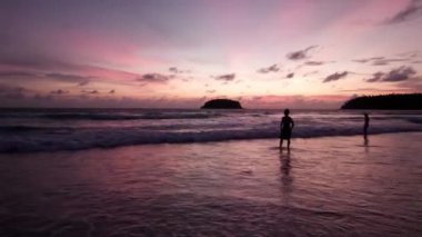 İnsanlar gün batımına adanın manzarasıyla hayran kalıyor. Okyanusta ıssız bir ada duruyor, dalgalar etrafında kıvrılıyor. Gökyüzünde pembe bulutlar. İnsanlar banyo yapar ve güneşi izler. Sahil tatili, Tayland