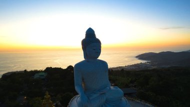 Büyük Buda, gün batımını seyrediyor. Phuket. İnsanlar heykele çıkan basamakları tırmanıyor. Adanın yeşil tepeleri her yerde. Uzakta, parlak güneş denizin üzerinde gider. Yukarıdan görüntüle