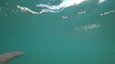 Adam sudan çıkar ve gün batımını seyreder. Elin görüntüsü, gökyüzünün yansıması olan yeşil su ve güneş ışınları. Küçük dalgalar. Deniz manzarası, büyük bulutlar ve sarı günbatımı.