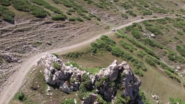 一辆白色的越野车沿着河边的峡谷越过了一条山路 有悬崖的绿地 路上陡峭的悬崖和大石头 陡峭的上坡 俯瞰群山 圣诞树 — 图库视频影像