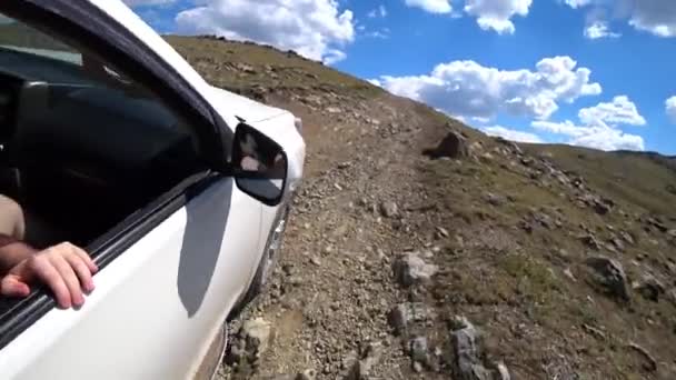开一辆越野车穿过群山 一辆白色的汽车驶过岩石 陡峭的斜坡和绿草 天空中有白云 车轮滑倒了 从路上的出租车上看 — 图库视频影像