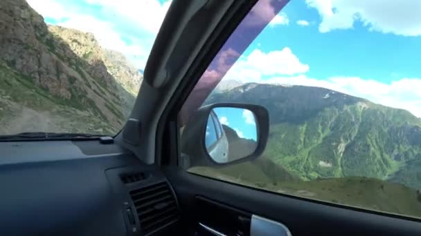 开一辆越野车穿过群山 一辆白色的汽车驶过岩石 陡峭的斜坡和绿草 天空中有白云 车轮滑倒了 从路上的出租车上看 — 图库视频影像
