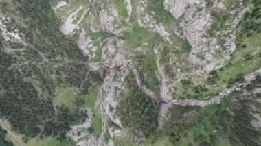 Bir dağ geçidinde yüksek bir şelale çağlıyor. Kozalaklı ağaçlar, Noel ağaçları ve otlar yetişir. Nehir akıyor. Yürüyüş yolları. İHA 'nın üst görüntüsü. Gün batımı. Burkhan Bulak Şelalesi, Kazakistan