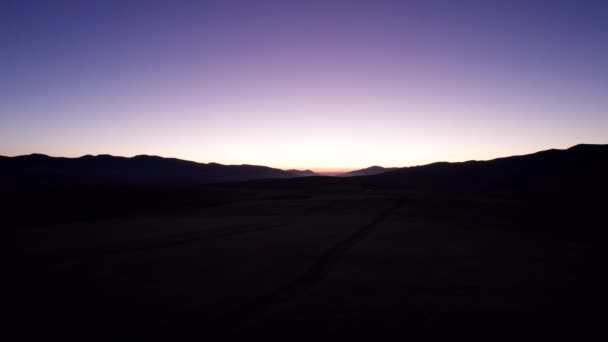 山で夜明けする ヴァイオレット オレンジ色の空 太陽の赤い光線はピークの後ろから出てくる ゴージャスに光が当たる 道路やプードルの痕跡が見える ドローンビュー — ストック動画