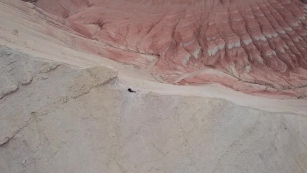 多彩的高山和由粘土制成的峡谷 一个有着不同岩石和不同颜色的大峡谷 岩石墙壁上的红色 白色和黄色的花 一个游客散步 Aktau — 图库视频影像