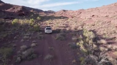 Bozkırdaki kırmızı dağların arasından beyaz bir SUV geçiyor. Cipin arkasında toz uçuyor. Çalılar büyür. Devasa taşlar ve bir sürü tepe var. Çöl. İnsansız hava aracının manzarası. Macera. Kazakistan