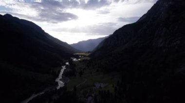 Yeşil vadi ve nehir manzaralı güzel bir gün batımı. Kozalaklı ağaçlar, ormanlar, bir sürü ot. Kaynayan gri bir nehir. Gökyüzündeki bulutlar. Güneş ışınları. Dik uçurumlar