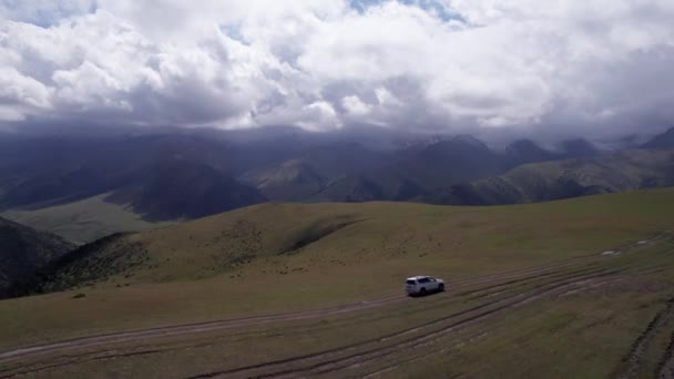 Suv는 산에서 운전하고 있습니다 거대한 산봉우리와 필드의 드론에서 더러운 오프로드와 — 비디오