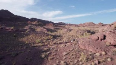 Bozkırdaki kırmızı dağların arasından beyaz bir SUV geçiyor. Cipin arkasında toz uçuyor. Çalılar büyür. Devasa taşlar ve bir sürü tepe var. Çöl. İnsansız hava aracının manzarası. Macera. Kazakistan