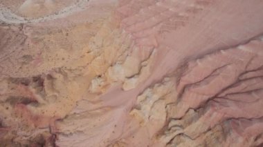 Renkli yüksek dağlar ve balçıktan yapılmış bir kanyon. Farklı taşları ve farklı renkleri olan büyük bir vadi. Kayaların duvarlarında kırmızı, turuncu, beyaz ve sarı çiçekler var. Bir turist yürüyor. Aktau