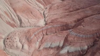 Renkli yüksek dağlar ve balçıktan yapılmış bir kanyon. Farklı taşları ve farklı renkleri olan büyük bir vadi. Kayaların duvarlarında kırmızı, turuncu, beyaz ve sarı çiçekler var. Bir turist yürüyor. Aktau