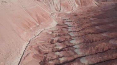 Renkli yüksek dağlar ve balçıktan yapılmış bir kanyon. Farklı taşları ve farklı renkleri olan büyük bir vadi. Kayaların duvarlarında kırmızı, turuncu, beyaz ve sarı çiçekler var. Bir turist yürüyor. Aktau