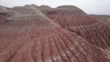 Renkli yüksek dağlar ve balçıktan yapılmış bir kanyon. Farklı taşları ve farklı renkleri olan büyük bir vadi. Kayaların duvarlarında kırmızı, turuncu, beyaz ve sarı çiçekler var. Bir turist yürüyor. Aktau
