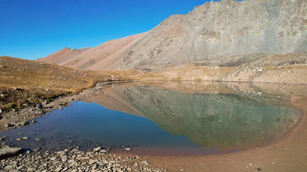 山の湖の水のエメラルド色 山の反射と緑の山の湖のドローンビュー 滑らかな透明水 近くに大きな石がある 乾燥草カザフスタン — ストック写真