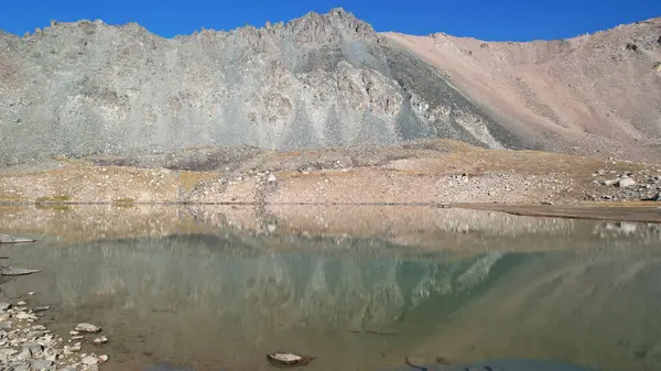 环绕着岩石的透明的山湖 水就像一面镜子 反射着岩石和斜坡 水面上的光波荡漾 底部是可见的 有很多大石头 — 图库照片