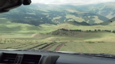 Güzel bir manzarası olan arabayla tehlikeli bir iniş. SUV yeşil çimlerle dik bir yokuştan aşağı iniyor. Dağlar ve ormanlar uzaktan görülebilir. Nehir akıyor. Gökyüzü bulutlarda.
